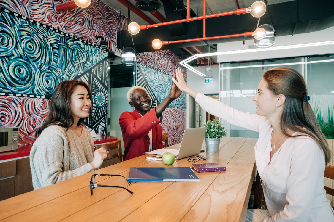 Group of positive young multiethnic female colleagues smiling and giving high five